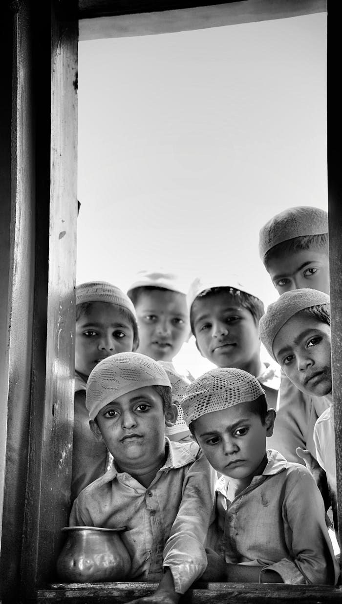 services-03 A group of children in traditional attire gazing through a window with solemn expressions.