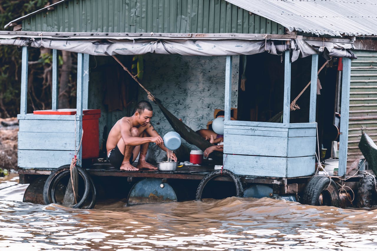 services-02 A man sits on a flooded wooden houseboat during a heavy flood.