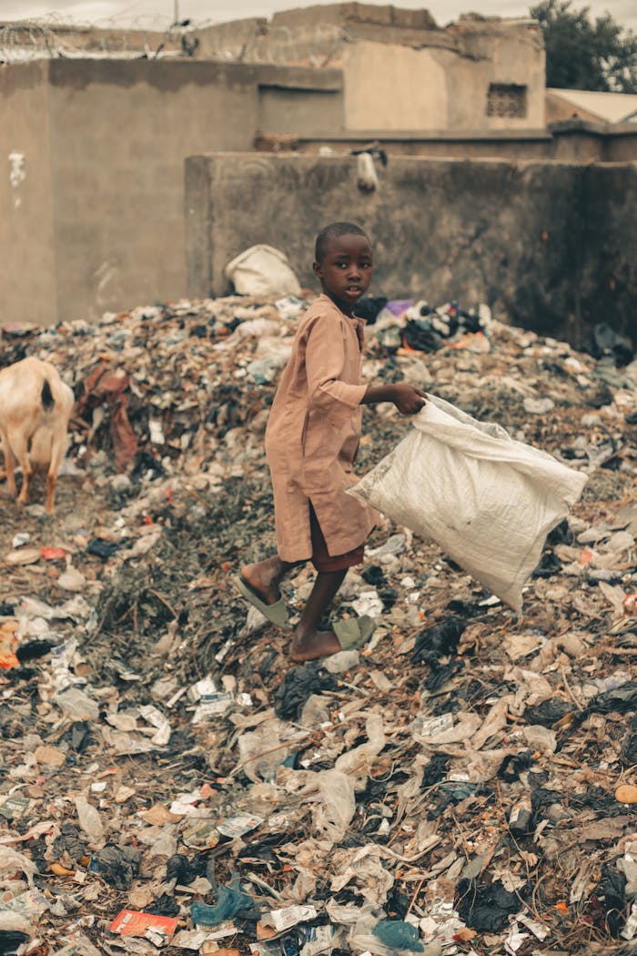 about-us Young boy in an urban area collecting recyclables amidst trash piles, highlighting environmental challenges.